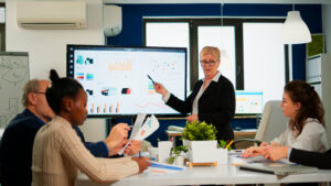 Chief analyst presenting a 24-month FATF 5th round preparation roadmap on a digital whiteboard to economists in a boardroom for Japanese institutions