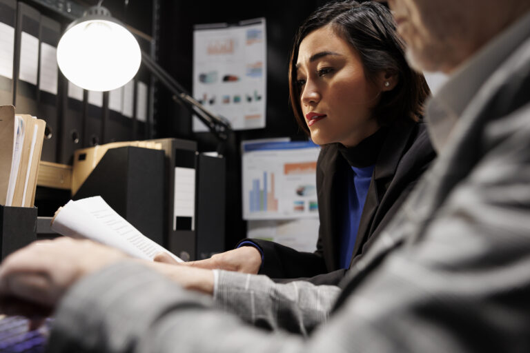 Elderly compliance executive and Asian colleague reviewing archived bookkeeping evidence for Japan's FATF effectiveness assessment documentation gaps
